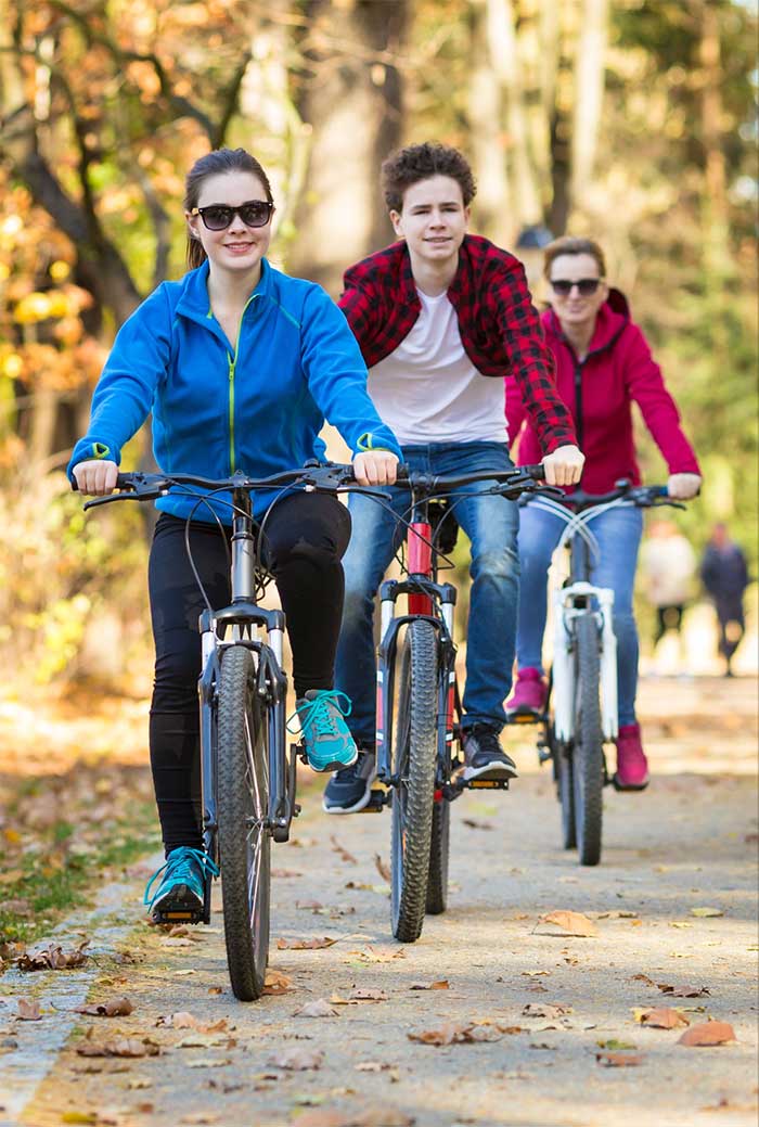 three people riding bikes on road with fallen leaves