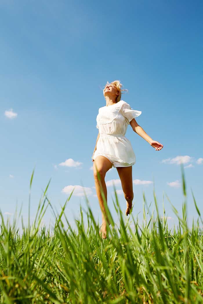 woman running through grassy field under blue sky