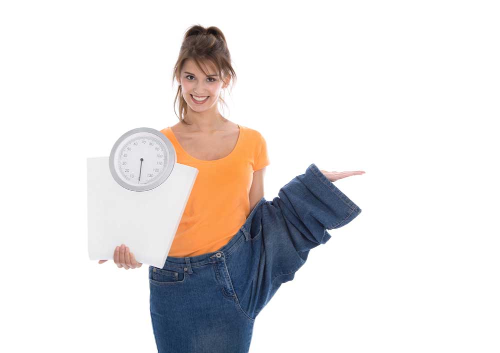 woman in orange shirt holding scale and wearing large pants